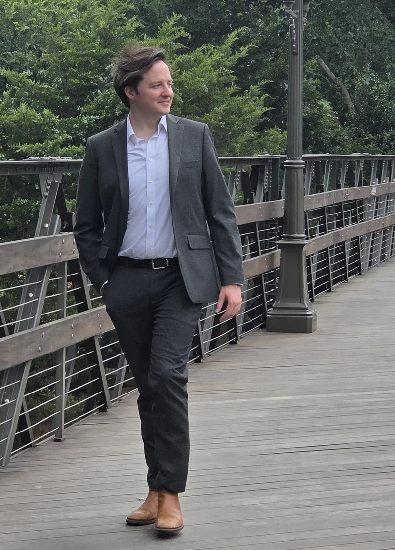 Flynn Peters walking across a footbridge in a gray blazer